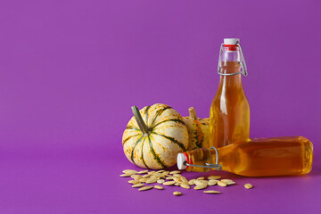 Bottles of tasty pumpkin seed oil on purple background