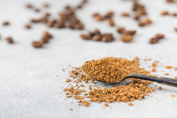Small spoon with instant coffee granules above grey stone table in light studio. Copy space