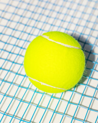 A yellow tennis ball on the blue strings of a tennis racket on a white background. Sport composition