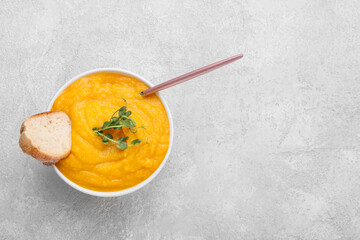 Bowl of tasty pumpkin cream soup with bread on grey background