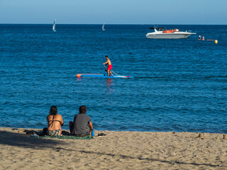 Una pareja sentada en la arena de la playa de Fuengirola mirando la practica del paddel surf