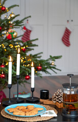 Gingerbread cookies, candles and teapot with hot tea in front of a decorated Christmas tree