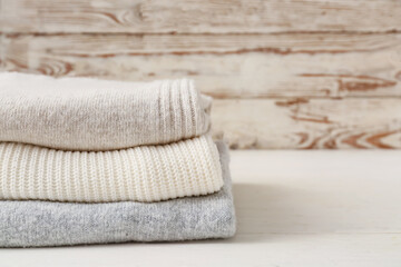 Fototapeta na wymiar Stack of different cozy sweaters on light wooden background