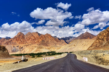 A concrete road towards beautiful rocky mountains and blue sky with peaks of Himalaya, Leh, Ladakh, Jammu and Kashmir, India