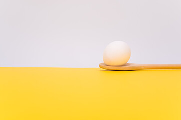white egg on a wooden spoon with white and yellow background