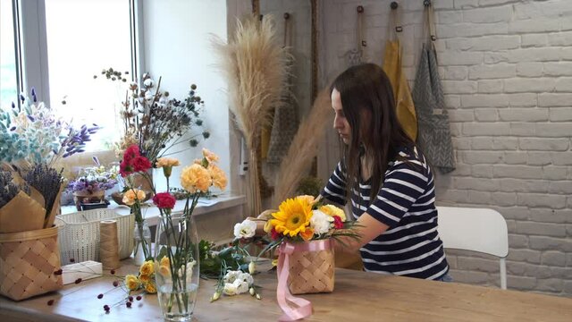 Process of creating bouquet in flower shop, close up. Woman hands working with basket and ribbon. Female florist create beautiful composition. Teacher of floristry in master classes.