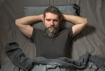 a gray-haired young man with a beard lies in bed at night and thinks. The concept of insomnia..