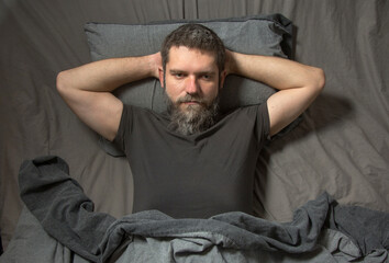 Obraz premium a gray-haired young man with a beard lies in bed at night and thinks. The concept of insomnia..