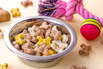 Brown biscuit bones and crunchy organic kibble pieces for dog feed with different toys on light background. Healthy dry pet food concept.