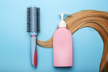 Shampoo bottle wrapped in lock of hair  and comb on a blue background