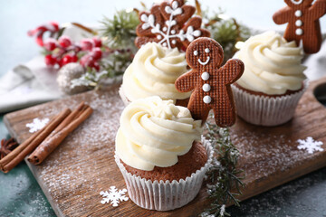 Wooden board of tasty Christmas cupcakes with gingerbread cookies and decor on table