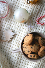 Bowl of cookies, soft knitted blanket and colorful Christmas ornaments at home. Flat lay.