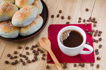 Cup of coffee and fresh fragrant buns with sesame seeds on a wooden table