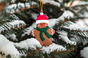 Christmas gingerbread man toy in Santa hat hangs on snow covered tree. Christmas tree toy. Snow covered Christmas tree.