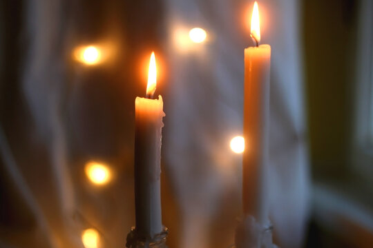 Two lit candles at night. Bokeh lights in the background. Selective focus.