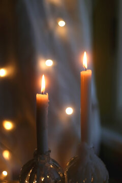 Two lit candles at night. Bokeh lights in the background. Selective focus.