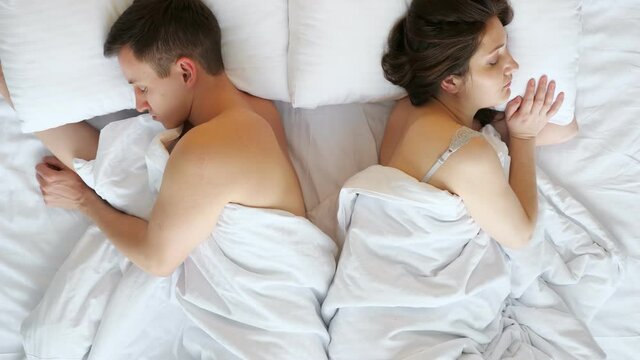 Couple Husband And Wife Sleep Turning Away After Argument In Bed On Soft Pillows Covered With White Sheets In Bedroom At Home Upper View.