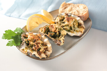 Baked oysters in Rockefeller style with spinach and cheese on a small plate with lemon, bread and parsley garnish as an festive appetizer, white table, copy space, selected focus