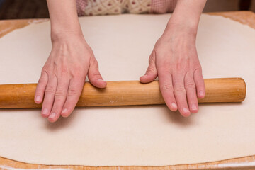 Female cook rolling dough with rolling pin. Closeup.