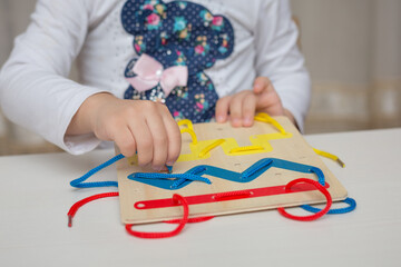 A child plays with a board with laces. Child development in the Montessori system.
