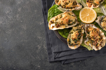 Oysters Rockefeller style baked with spinach and cheese on a plate with lemon and lettuce, dark slate background with copy space, view from above