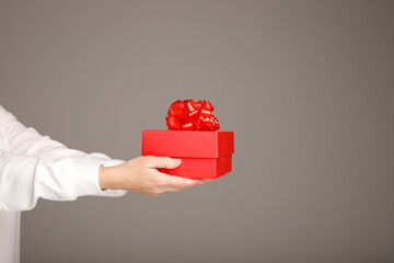 Female hands holding red gift box with red ribbon on grey background. Present for birthday, valentine day, Christmas, New Year. Congratulations background copy space.