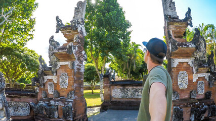 A young man taking a selfie under the entrance to Hindu temple in Lombok, Indonesia. The gate has...