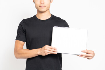 白い背景の前に立って小さいスケッチブックを見せる黒いTシャツを着ている男性