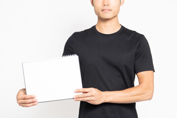 白い背景の前に立って小さいスケッチブックを見せる黒いTシャツを着ている男性