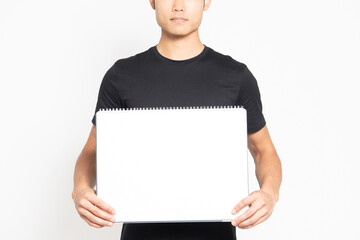 白い背景の前に立って大きいスケッチブックを見せる黒いTシャツを着ている男性