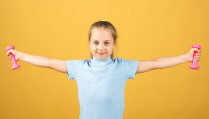 Fitness child. Portrait of sporty little girl with dumbbells over yellow studio isolated background. Gym workout. Child sportsman, childhood activity. Kids sport and Fitness.