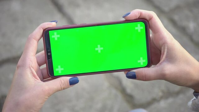 Woman holds mobile phone and clicks on screen swipes photos or pictures on street on background of paving slabs. Chroma key mock-up on smartphone in hand. Use green screen for copy space closeup 4k