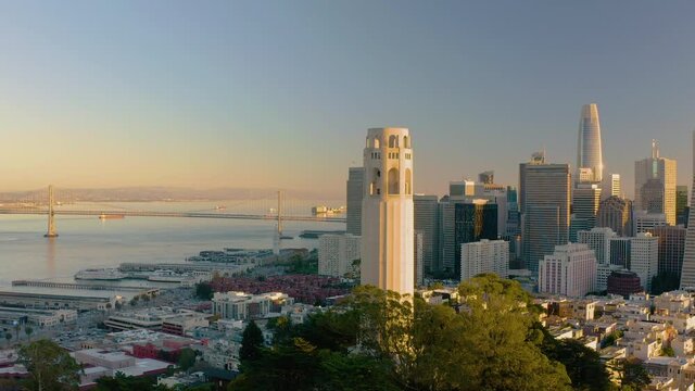 4K aerial video footage of San Francisco, California at sunset. View is stationary in front of famous tower in North Beach. Golden light on tower, Bay Bridge in the background.