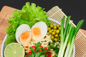 Beautiful Noodle Dish with Green Onions, Eggs, Green Pea, Red Hot Pepper, Greens and Lime on Sushi Mat. Instant Noodles with Vegetables