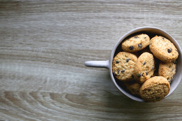 Ceramic bowl filled with chocolate chip cookies on wooden table. Flat lay.