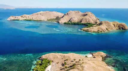 A drone shot of two bigger paradise islands in Komodo National Park, Flores, Indonesia. The islands have scarcely any trees and bushes. Dry land. Idyllic white sand beaches. Island hoping