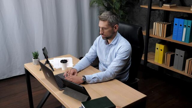Focused adult man stock trader broker distance works for laptop typing text on keyboard in office. Male businessman sitting on chair at desk uses computer online chatting with company investors
