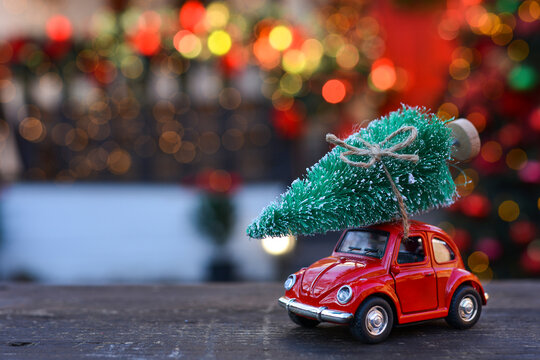 Retro toy red car carrying tiny Christmas tree on the background of christmas bokeh. Christmas cards. Trucking.Delivery service. Copy space