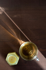 top view of a mug of tea and a jar of honey with sunny shadows on a wooden table. place to insert text