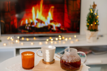 On side table tea cup, teapot and candle with fireplace on background