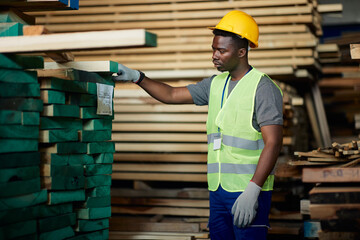 Young black man works with wood planks at lumber distribution warehouse.