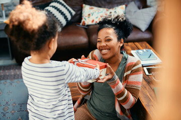 Happy African American mother receives present from her daughter at home.