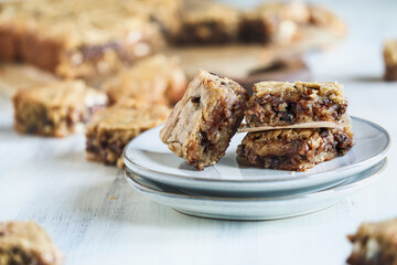 Fresh made homemade fudgy blondies or vanilla brownies stacked on a saucer over a white rustic wooden table. Extreme shallow depth of field with blurred foreground and background. - obrazy, fototapety, plakaty