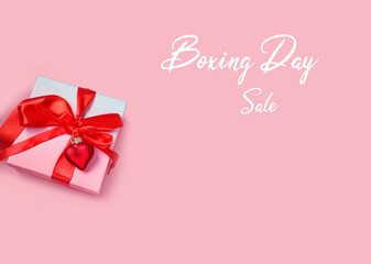 Boxing Day Sale. gift box with red ribbon and heart shape decor on pink background. concept of Boxing day, winter seasonal christmas  offer promotion advertising. top view