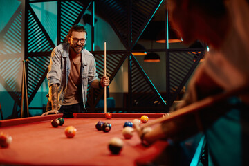 Young smiling man enjoys in snooker game with his girlfriend at pub.