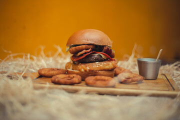 burger with onion rings
tasty with appetizers such as fried onion rings with white garlic sauce. Juicy burger with bacon and cheddar cheese on a rustic dark wood background.