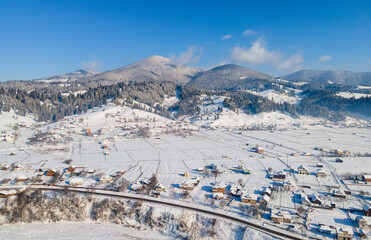 Aerial winter landscape with small village houses between snow covered forest in snow mountains 