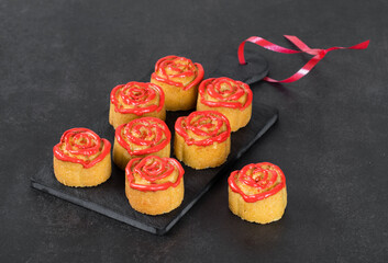 Dessert Cookies cakes in the shape of a rosebud with red icing sugar on a serving board on a dark gray background