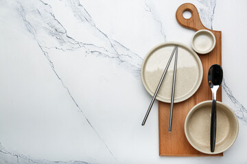 empty plates of different sizes on a cutting board with chinese chopsticks on a white background with space for text