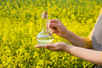A woman stands in a rape field and holds a glass bottle or jug of rapeseed oil in his hands....